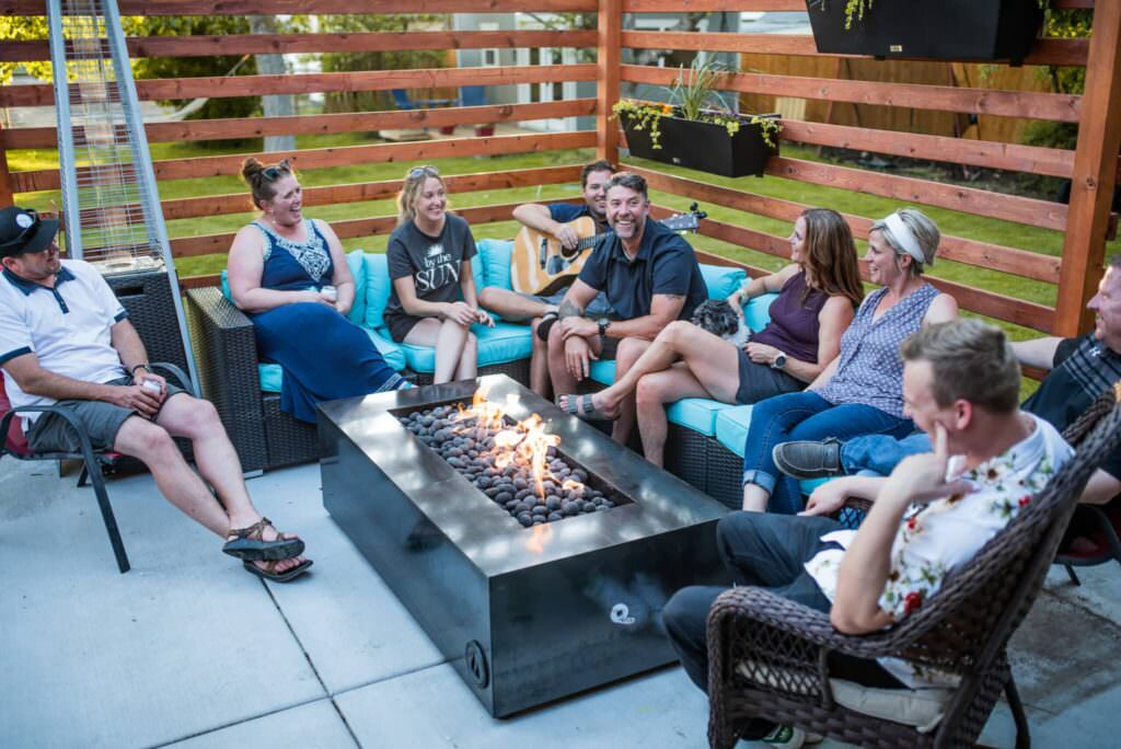 Group of people sitting on a sectional around a black rectangular fire pit with large flames