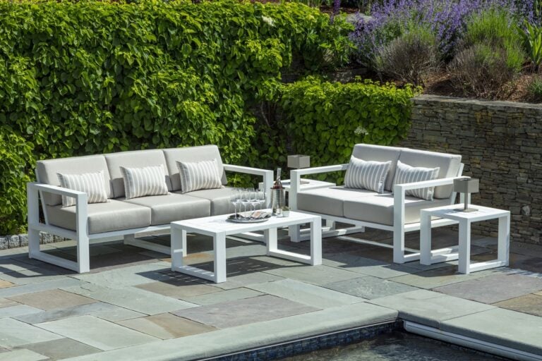 white and linen outdoor couch and loveseat with end tables located near a pool with greenery