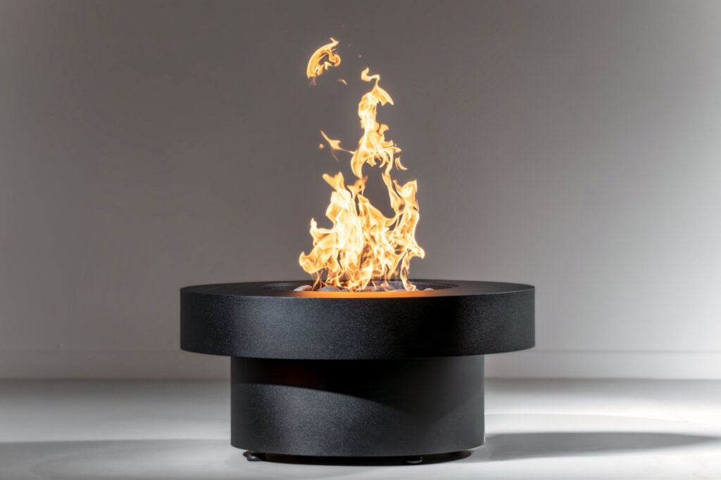 large, black, round, steel gas fire pit known as the Badlands with tall flames in white studio